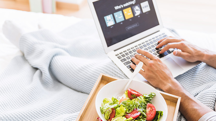 Hombre viendo Netflix en computadora con desayuno en cama