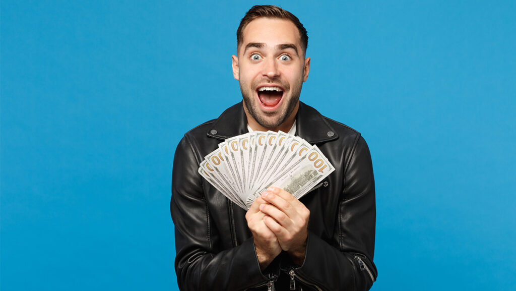 Hombre sonriente sorprendido con billetes en la mano y chamarra negra