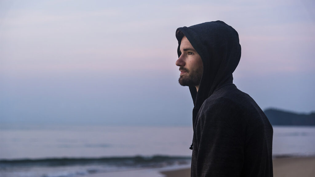 Hombre joven con sudadera viendo el mar