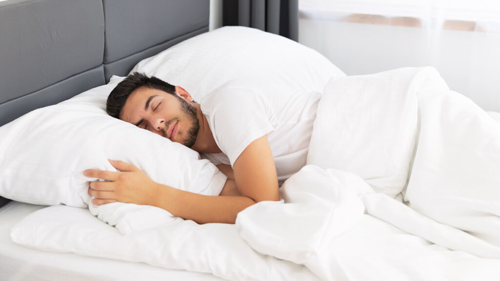 Hombre durmiendo en cama con sábanas blancas