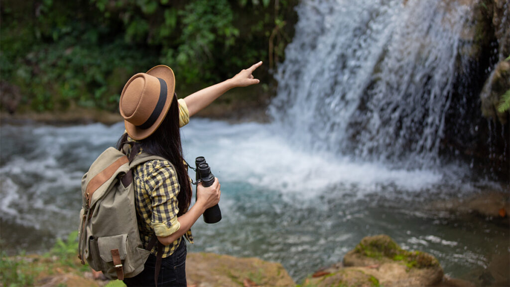 Mujer con sombrero y binoculares viendo una cascada