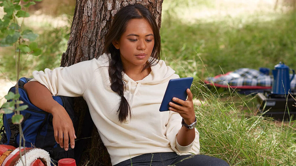 Mujer apoyada en un árbol leyendo y aprovechando las características del nuevo Amazon Kindle 2022