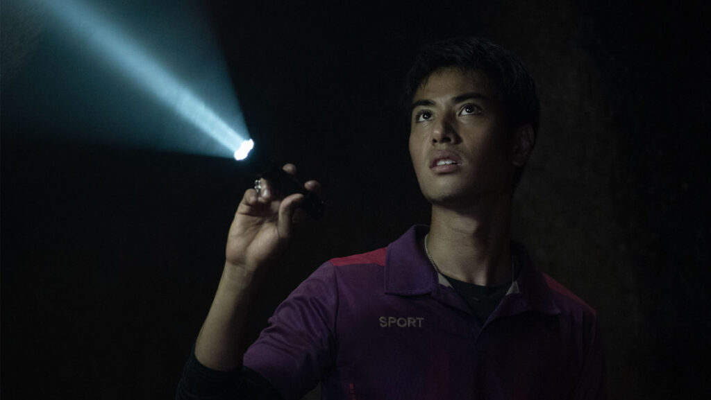 Joven iluminando con linterna al interior de una cueva