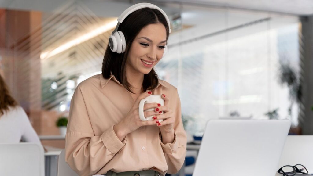 Mujer con audífonos y taza de café frente a su computadora