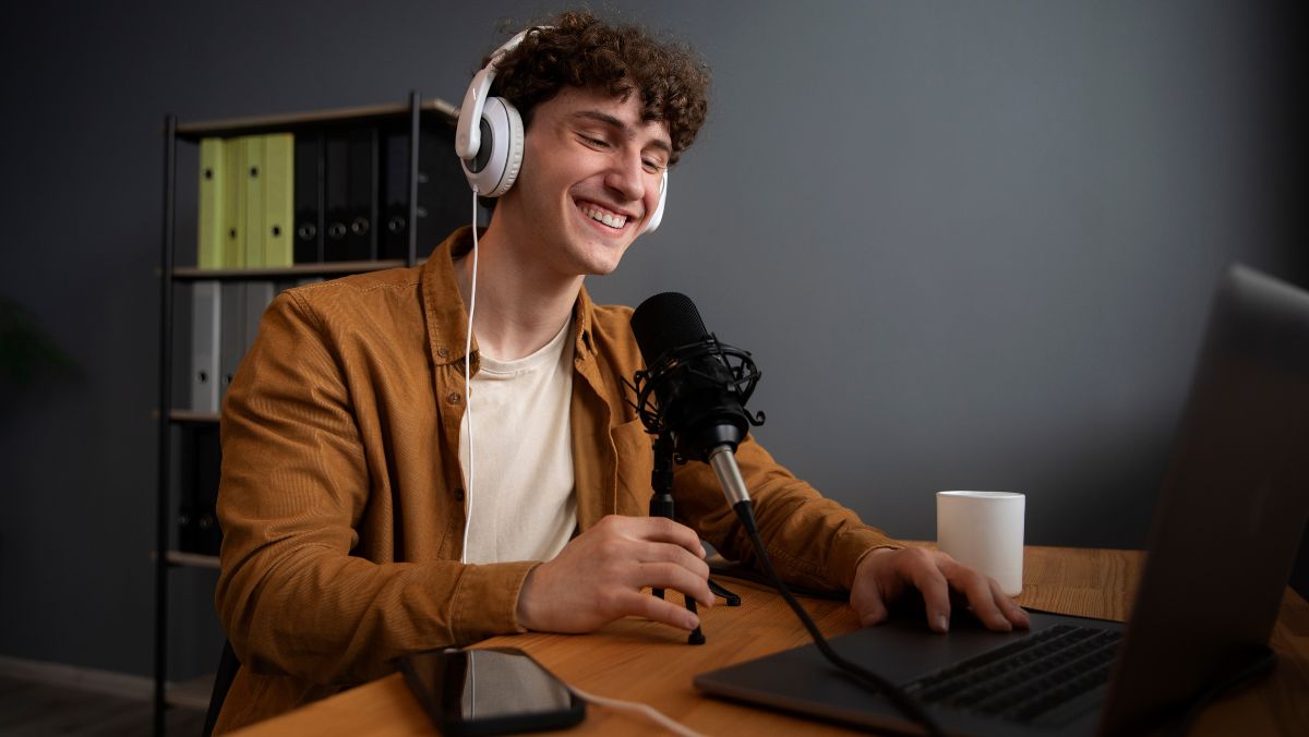 Hombre joven con audífonos y un micrófono delante de una laptop