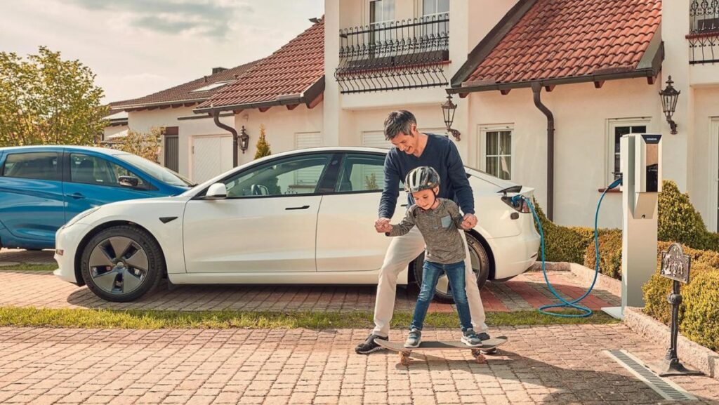 Papa con niño frente a casa con cargador de auto eléctrico