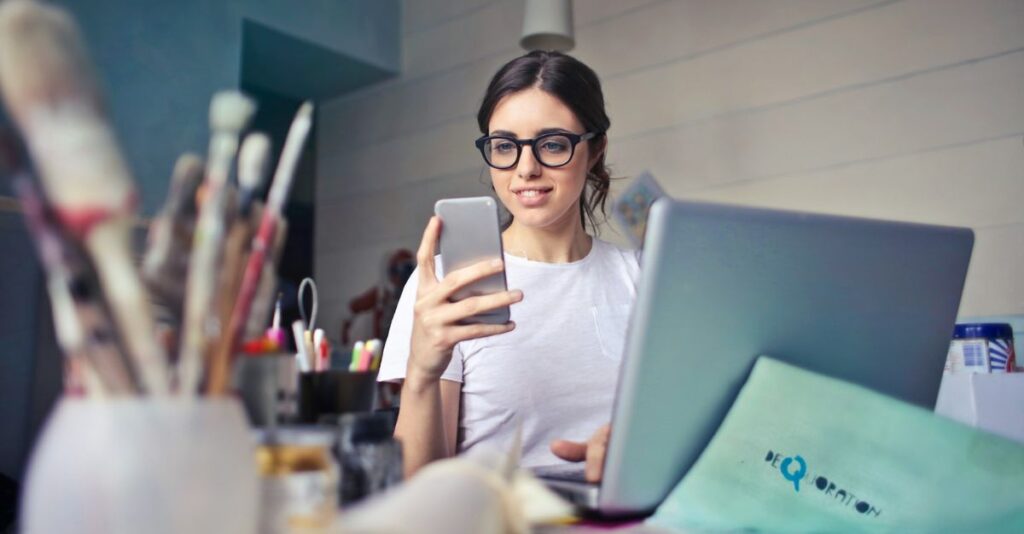 Joven revisando celular con laptop abierta